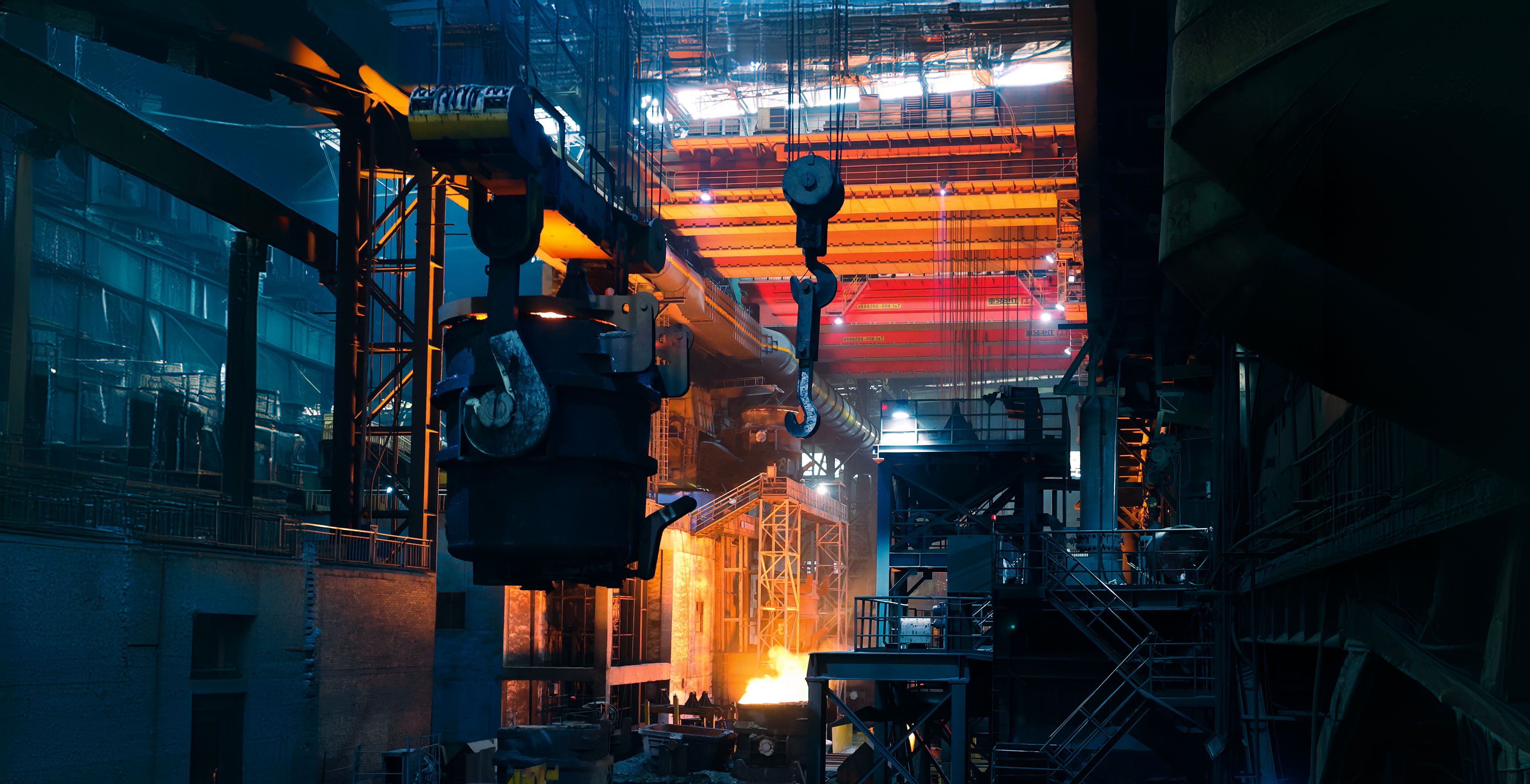 A dramatic industrial scene inside a steel mill or factory, with overhead cranes, gantry systems, and bright orange molten metal glowing at the bottom center.