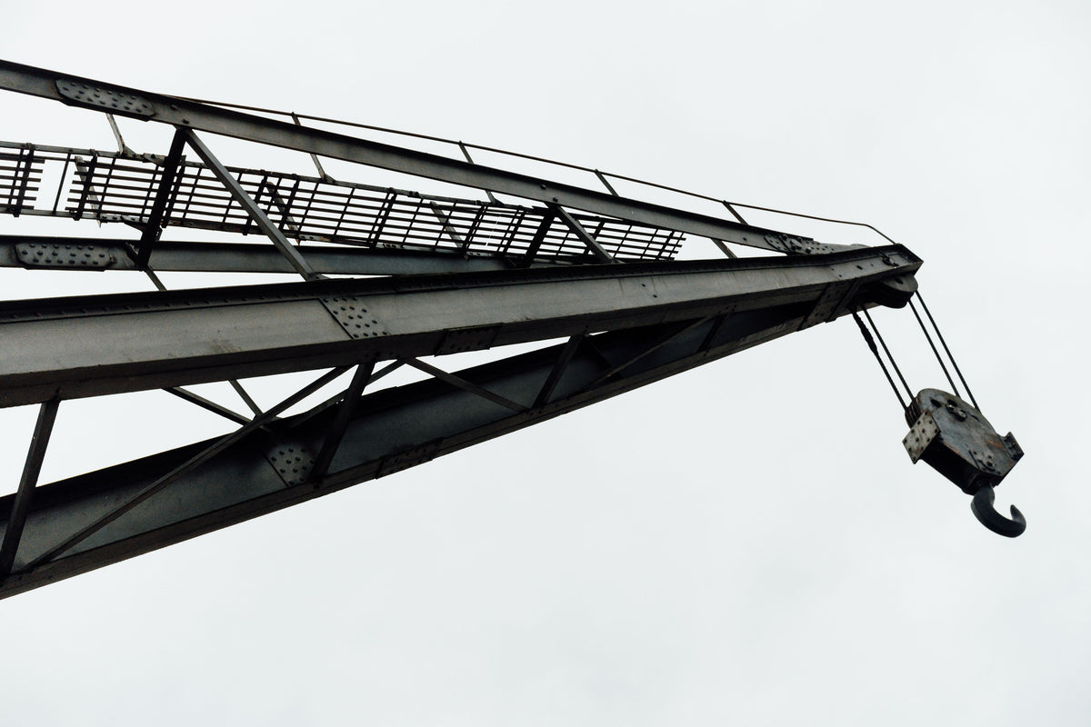 Close-up of a large steel crane arm and hook against a pale gray sky.