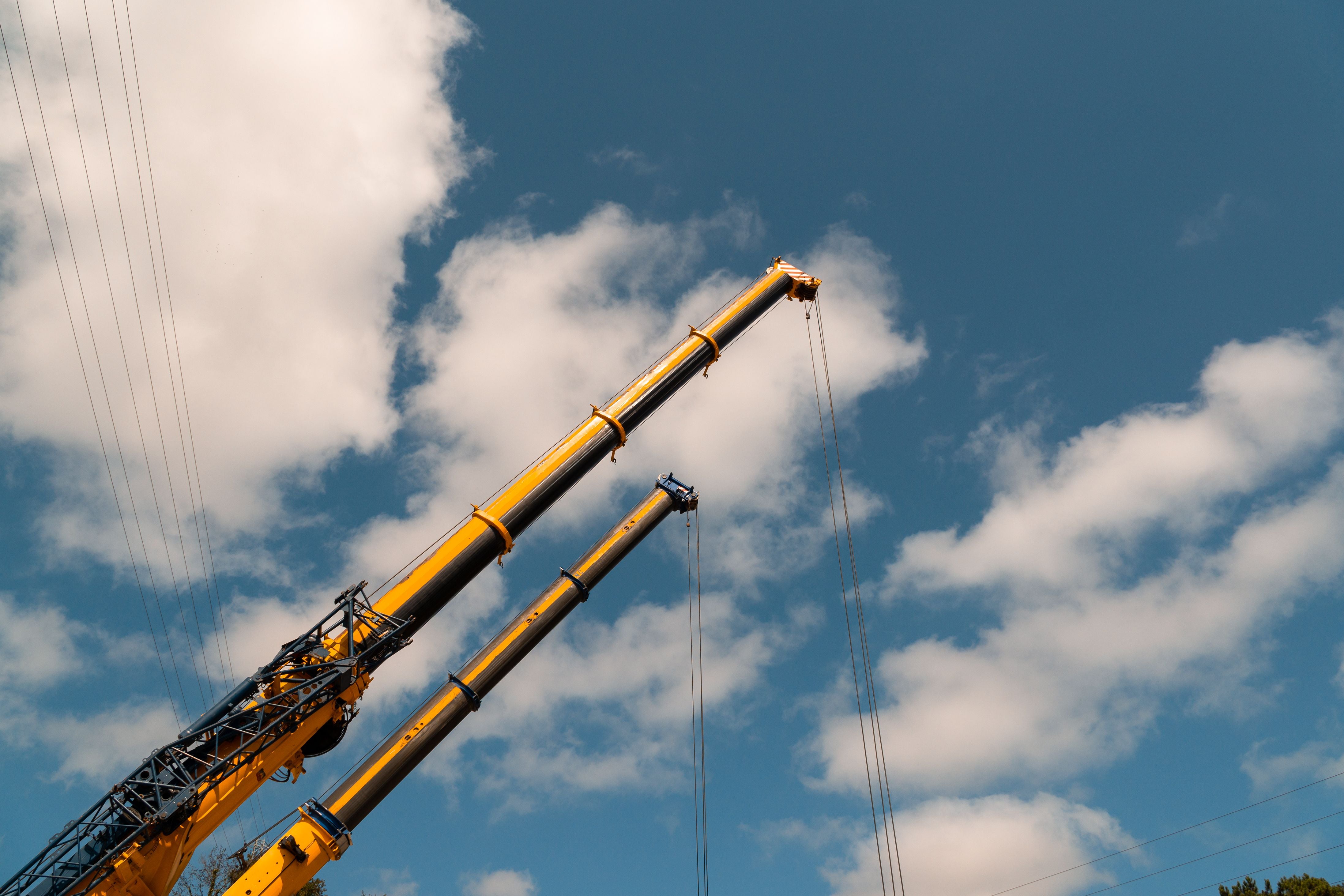 Yellow construction cranes with long boom arms reaching upward against a bright blue sky with scattered white clouds.